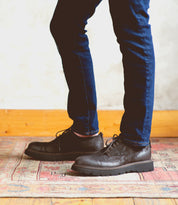 A man wearing jeans and a pair of Bed Stu Grant, standing on a rug.