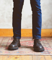 A man's feet clad in Bed Stu Grant shoes stand confidently on a handcrafted rug. The combination of Italian leather and meticulous craftsmanship ensures durability in every step taken.