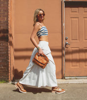Woman in summer attire with a Bed Stu Greenway crossbody strap walking past an orange door.