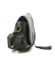 Bed Stu’s Half Moon EM is a black leather saddlebag crossbody purse featuring stitched edges, brass hardware, and a leather tassel zipper pull, shown at an angle to highlight its side and strap.