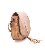 The Bed Stu Half Moon EM is a small tan leather crossbody purse with a flap closure, visible stitching, metal hardware, a tassel accent, and an elegant embossed foliage pattern for texture.
