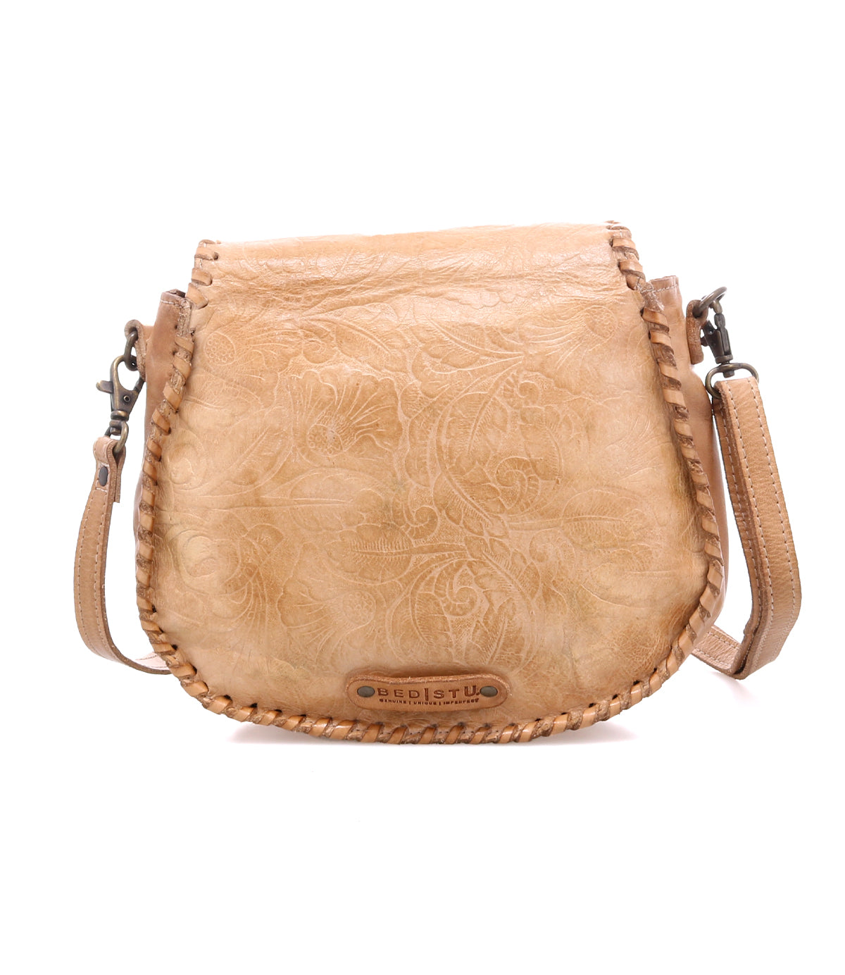 The Bed Stu Half Moon EM is a tan leather saddlebag crossbody purse featuring an embossed foliage pattern, braided edges, and an adjustable shoulder strap.