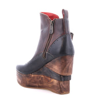 The Bed Stu Harmonious is a brown leather platform wedge ankle boot featuring a sculptural wood wedge, visible side zipper, striking red leather interior, and a wooden platform sole.
