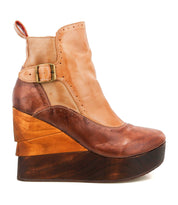 The Bed Stu Harmonious is a brown and tan platform wedge ankle boot with a leather upper, brogue perforations, buckle detail, and a layered sculptural wood wedge sole.