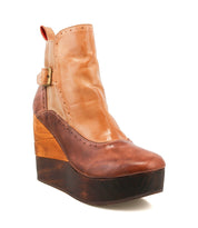The Bed Stu Harmonious is a brown and tan leather platform wedge ankle boot featuring brogue perforations, a buckle accent, and a sculptural wooden wedge sole.