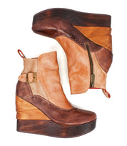 The Bed Stu "Harmonious" boots are two-tone leather platform wedge ankle boots with sculptural wood wedges, side zippers, buckles, and brogue perforations, shown against a white background.