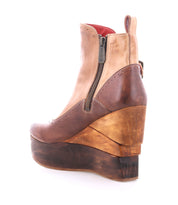 The Bed Stu Harmonious is a high-heeled platform wedge ankle boot with a sculptural wood wedge sole, brown and tan leather upper, side zipper, and bold red leather interior.