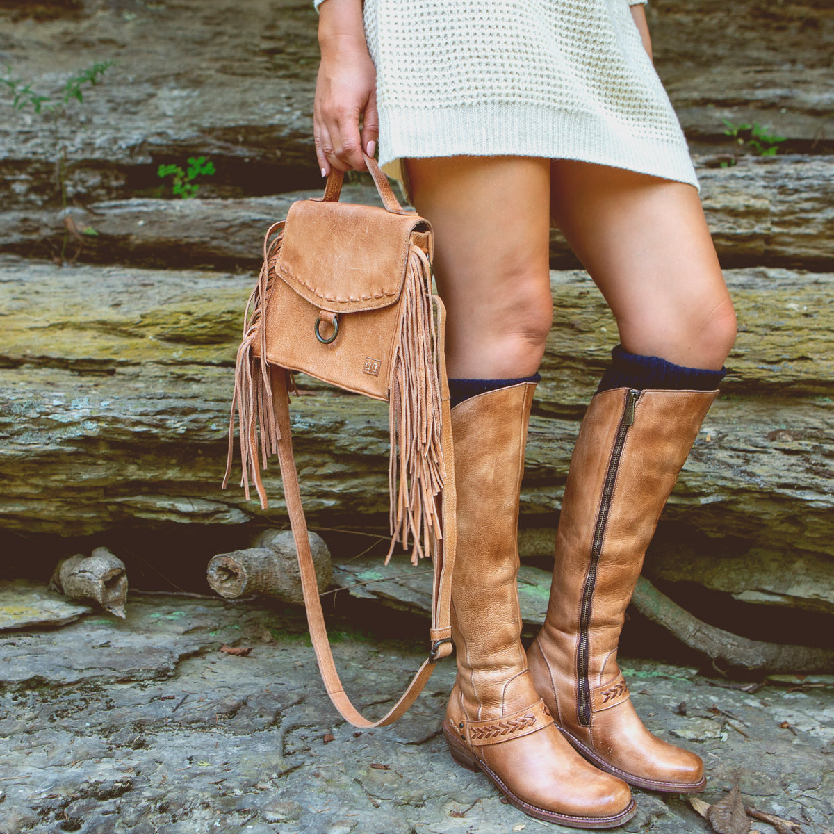 A woman wearing tan boots, a white sweater, and a Bed Stu Hidden adjustable compact leather crossbody bag.