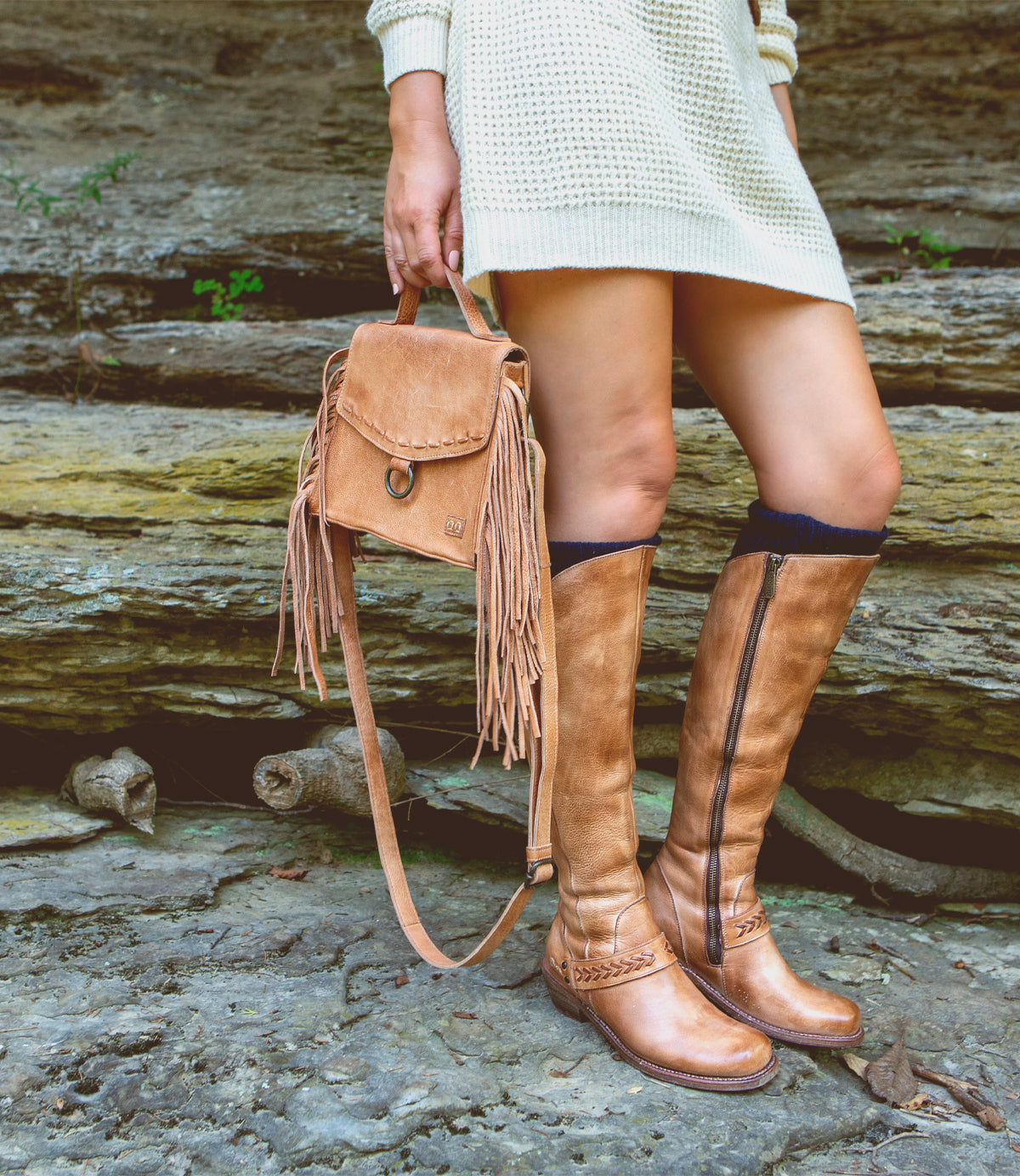 A woman wearing tan boots, a white sweater, and a Bed Stu Hidden adjustable compact leather crossbody bag.