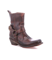 The Bed Stu Homage is a single worn brown leather ankle boot featuring a strap and buckle detail, low heel, and slightly pointed toe, reminiscent of a classic harness boot, shown on a white background.