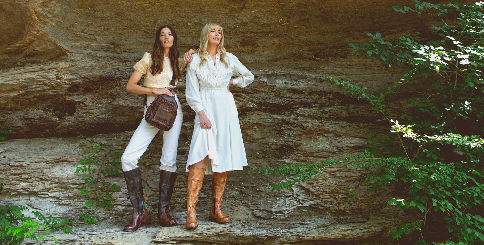 Two women in neutral outfits, standing on a rock ledge wearing tall leather boots 