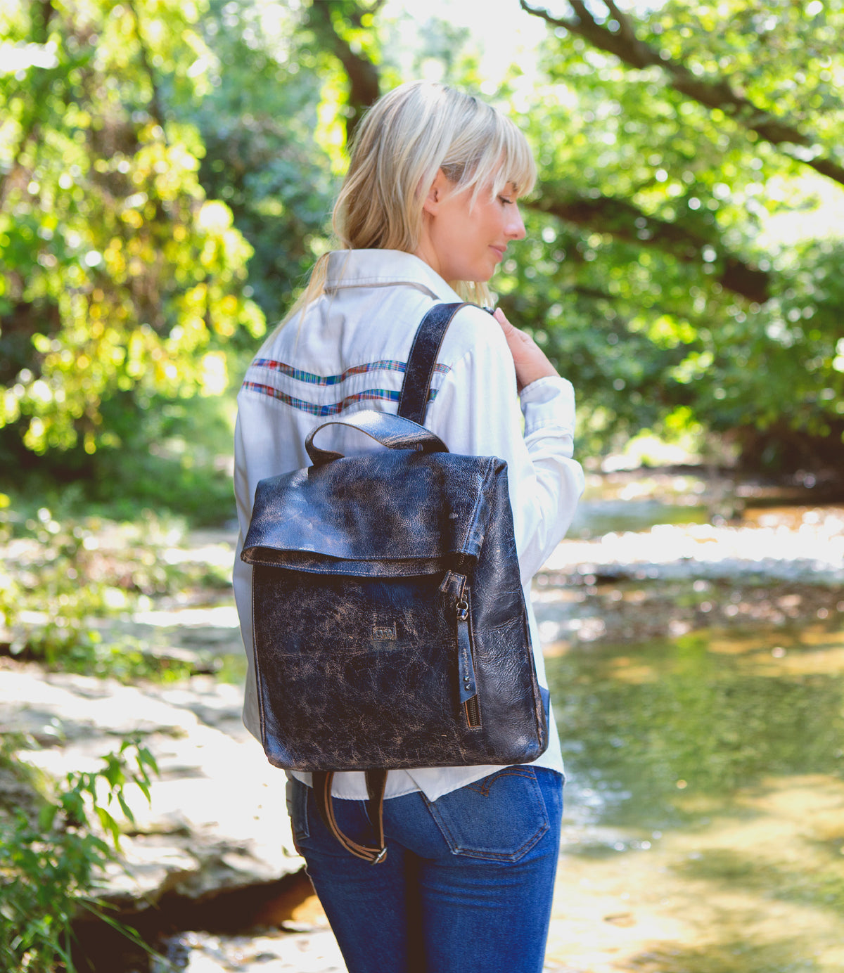 A woman standing by a river with a Bed Stu leather backpack named Howie.