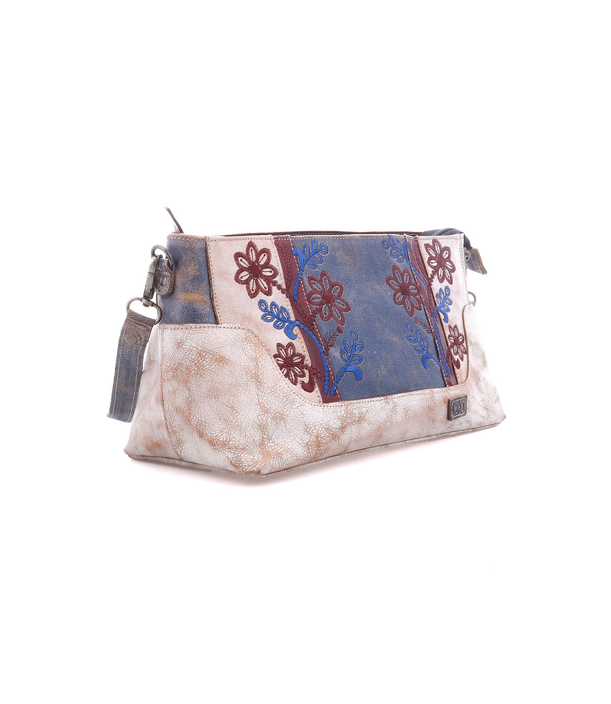 The Bed Stu Hyperbolic is a rectangular beige leather shoulder bag with a blue and maroon floral embroidered panel, side zipper, and bohemian handcrafted style, shown on a white background.