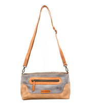 The Bed Stu Hyperbolic is a two-tone bohemian leather shoulder bag with an adjustable strap, front zipper pocket, and handcrafted logo patch on the front.