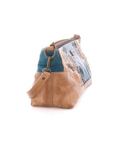 The Bed Stu Hyperbolic is a handcrafted tan and blue leather shoulder bag with floral embroidery, shown from the side, featuring a relaxed design, shoulder strap, and metallic hardware.
