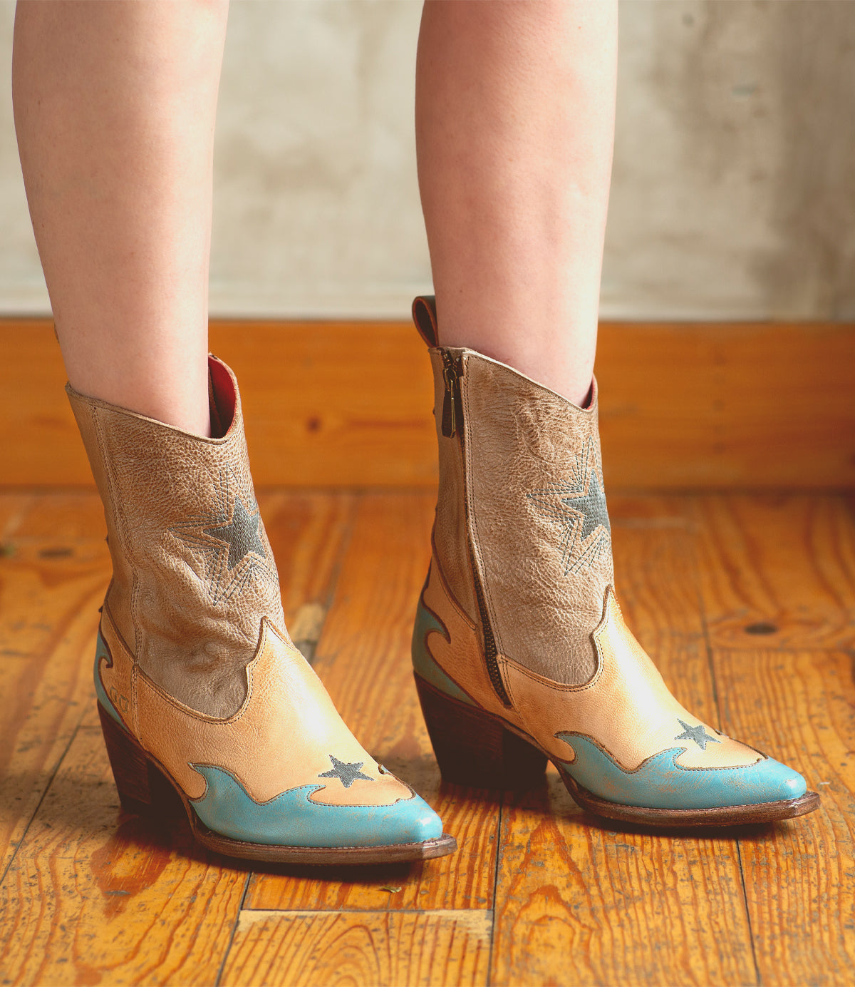 An artistically crafted pair of Hyperspeed boots, in shades of blue and tan, by Bed Stu, worn by a woman.