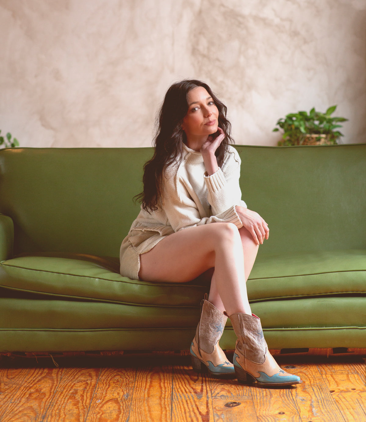 A woman sitting on a green couch wearing Bed Stu Hyperspeed leather boots.