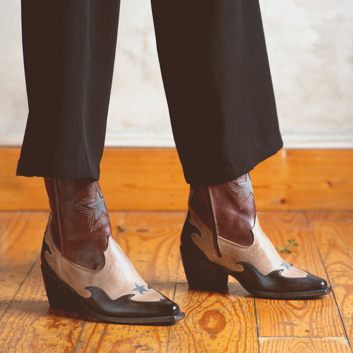 A woman wearing a handcrafted pair of Bed Stu Hyperspeed leather boots on a wooden floor.