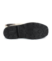 The image showcases the bottom view of Bed Stu's Illicit platform ankle boot, emphasizing its textured black rubber sole with deep treads and a touch of retro style.