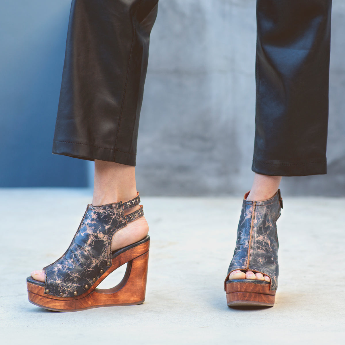 Imelda, a woman known for her incredible shoe collection, confidently struts in her Bed Stu leather pants paired with exquisite Bed Stu wooden wedges featuring an alluring open-toe design.
