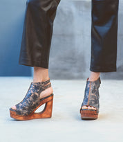 Imelda, a woman known for her incredible shoe collection, confidently struts in her Bed Stu leather pants paired with exquisite Bed Stu wooden wedges featuring an alluring open-toe design.