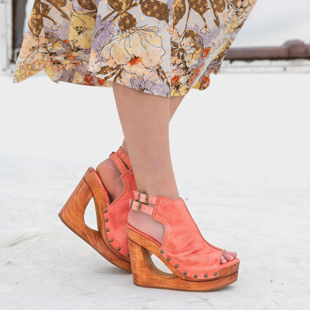 Bed Stu, a woman wearing a floral dress and wooden sandals with an open-toe design.