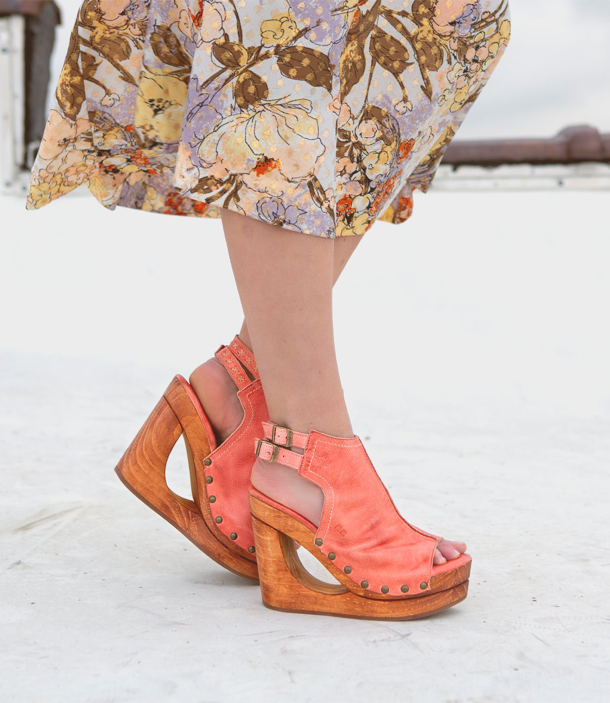Bed Stu, a woman wearing a floral dress and wooden sandals with an open-toe design.
