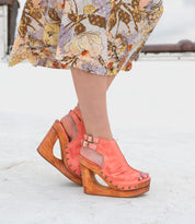 Bed Stu, a woman wearing a floral dress and wooden sandals with an open-toe design.