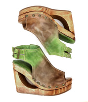 The Imelda by Bed Stu are brown and green wedge sandals with metal studs, wooden platforms, and distinctive cutout details in an open-toe design.