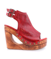 Introducing the Imelda by Bed Stu: a red leather wedge sandal with an open-toe design, incorporating double ankle straps with buckles, a wooden platform, and embellished with decorative metal studs.
