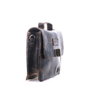 The Bed Stu Improv is a dark brown leather satchel with a flap closure, side metal ring, and top handle—combining fashion and functionality for a timeless look, shown upright on a white background.