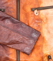 Close-up of Bed Stu's Include jacket—a handcrafted leather piece with metal zippers, detailed sleeves, and contrasting brown hues. This modern silhouette is a true statement from the iconic brand.