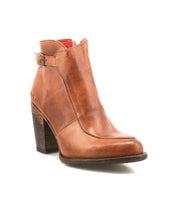 The Bed Stu Isla bootie is shown on a white background, featuring brown leather, a chunky wooden heel, vintage buckle detail, and a slightly pointed toe.