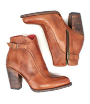 The Bed Stu Isla booties are brown leather ankle boots with side zippers, a vintage buckle, and stacked wooden heels, shown on a white background.