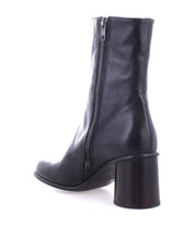 The Isodora ankle boot from Bed Stu, crafted in black Italian leather, showcases a back view highlighting its side zipper and block heel along with an asymmetrical toe.