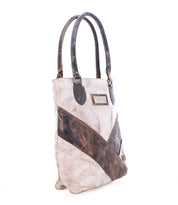The Italic by Bed Stu is a tan leather tote bag with dark brown diagonal and vertical patches, organic cotton twill accents, and two handles, standing upright against a white background.