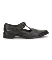 The image shows the Bed Stu "Jenny"—a single black leather T-strap shoe with a low heel, cushioned insole, side buckle, and rounded toe—displayed in profile against a white background.
