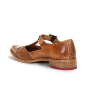 The Bed Stu Jenny is a brown leather casual shoe featuring a closed, T-strap pointed toe, low heel, cut-out design, and buckle strap, shown from the back left side.