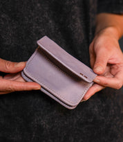 A person holds the Jeor wallet by Bed Stu, a small light purple leather accessory with stitched edges and multiple credit card slots, in both hands.