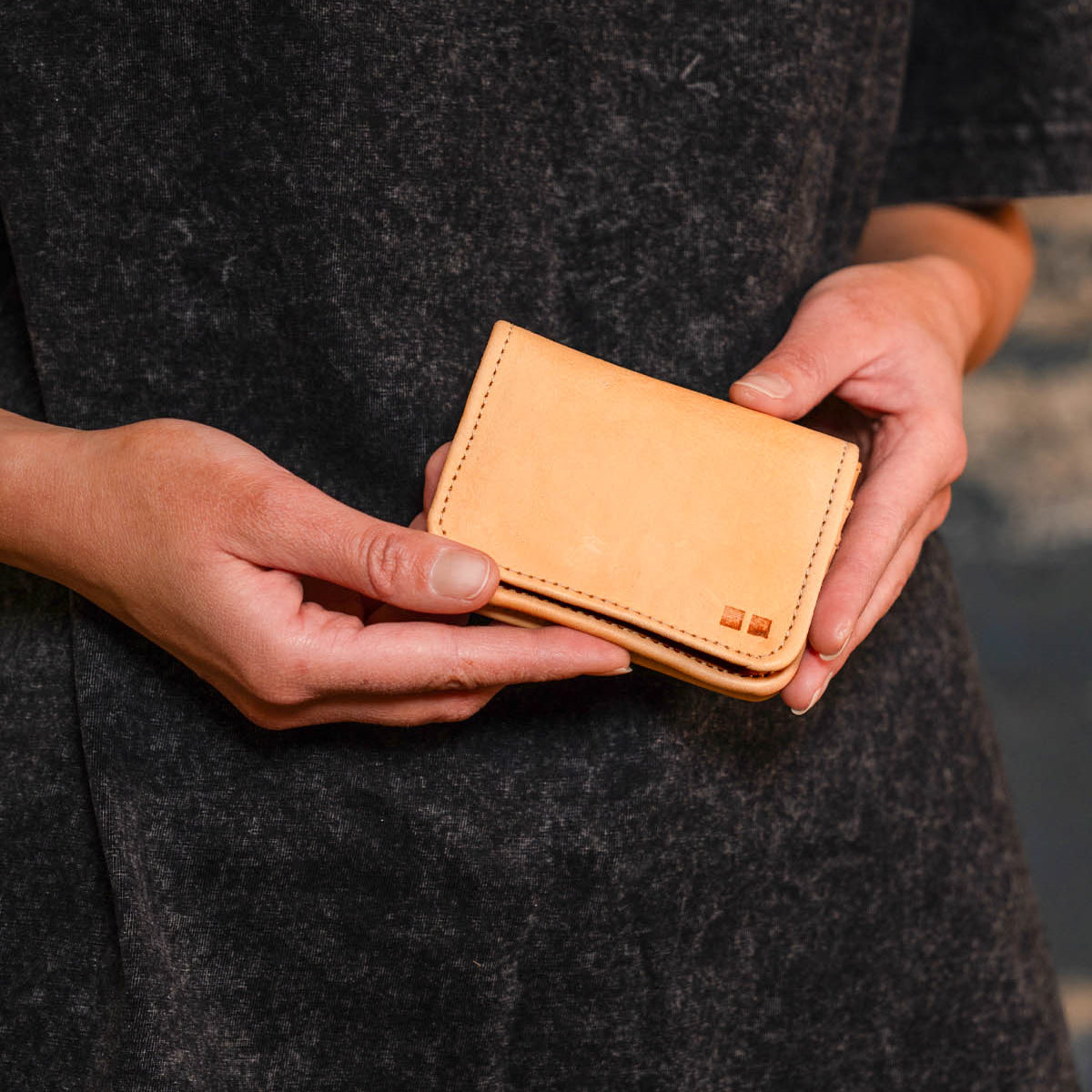 A person holds the Jeor leather card holder by Bed Stu with both hands against a dark gray background, showcasing its convenient credit card slots for easy organization.