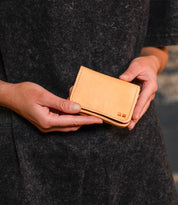 A person holds the Jeor leather card holder by Bed Stu with both hands against a dark gray background, showcasing its convenient credit card slots for easy organization.