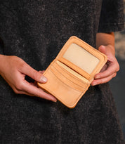 A person holds the Bed Stu Jeor, an open rustic leather card holder with visible credit card slots and a clear ID holder.