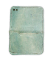 The Bed Stu Jeor is a light blue rustic leather card holder with visible stitching, an open pocket, and two small rectangular marks in the top left corner.
