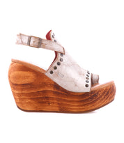The Joann II by Bed Stu is a modern white leather peep-toe wedge sandal with a wooden platform sole, adjustable back strap, and metal stud accents.