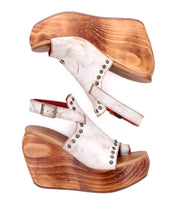 Bed Stu Joann II high wooden wedge platform sandals feature distressed white leather uppers, ankle straps, and metal stud accents, displayed side by side on a white background for an effortless touch of elegance.