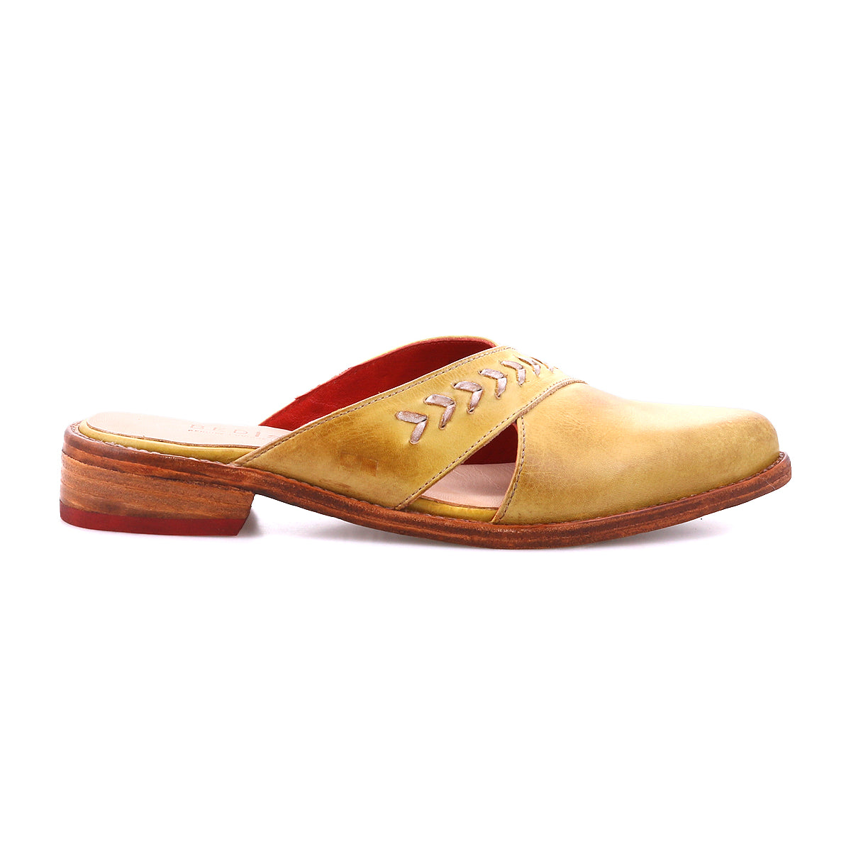The Bed Stu Jockey is a yellow-brown leather slip-on mule featuring a wooden sole, red interior lining, cut-out sides, pointed toe, and decorative stitching for a sleek look.
