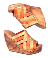 The Bed Stu Josie II is a pair of wooden wedge sandals with hand-woven orange and gold leather straps and metal stud accents.