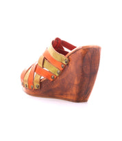 The Bed Stu Josie II is a wooden wedge sandal with a platform heel, showcasing hand-woven orange and yellow leather straps finished with metal studs.
