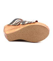 The Josie II by Bed Stu is a wooden wedge sandal with a light brown sole, black and metallic upper straps, and chic metal stud accents, shown from the bottom for added detail.