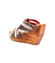 The Bed Stu Josie II is a single wooden wedge sandal featuring hand-woven leather crisscross straps and metal stud accents, shown against a white background.